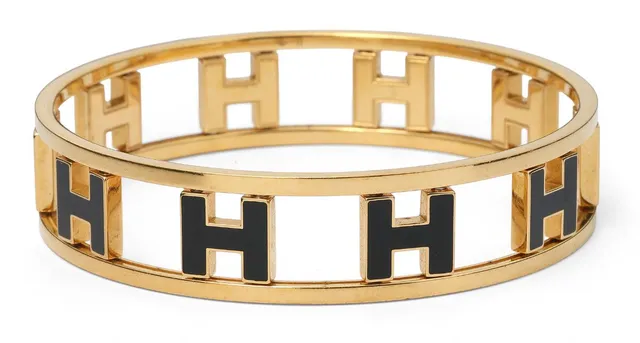 A “Rondo Ash H” bangle set in gold-toned metal with an “H” motif in black enamel. Weight app. 40.8 g. W. 1.6 cm. Inner diam. app. 6.6 cm.