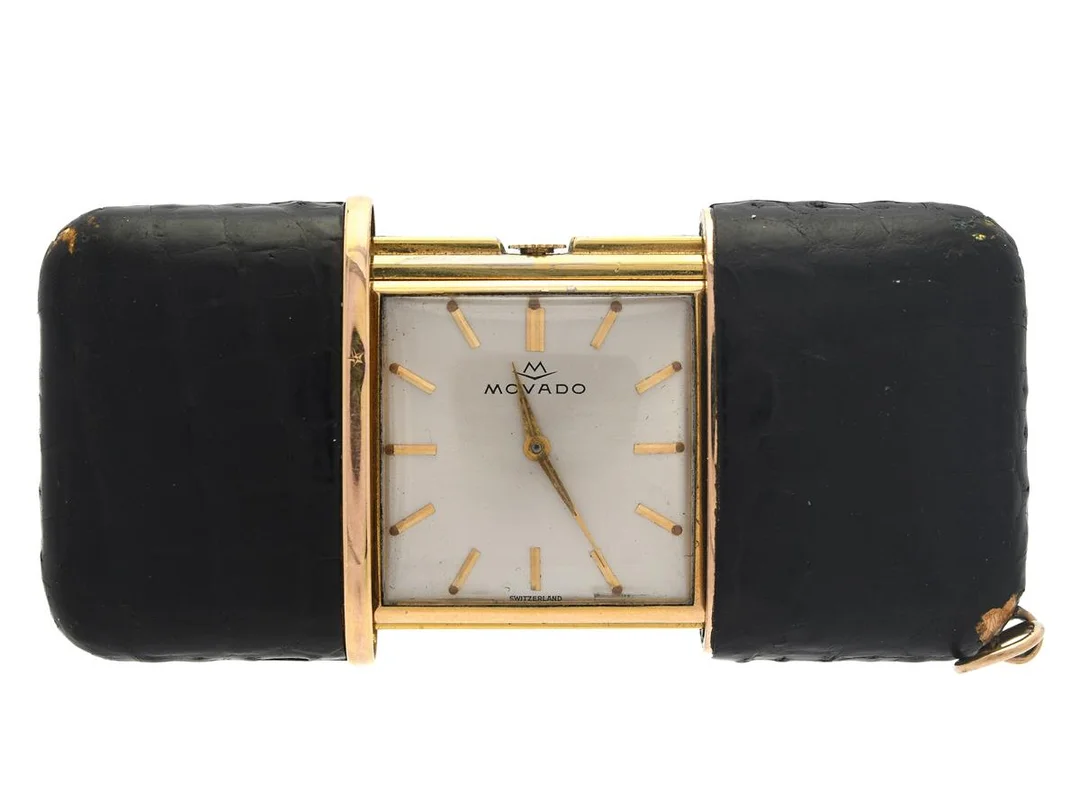 MOVADO, Ermeto, Boett nr. 1 352, reseur, 34,5 x 48 (73) mm, gulmetall/läder, manuell, plexiglas, skadad urtavla, ca 1960, Klockan dras upp genom att öppna och stänga fodralet. — Klockor/Movado — Kaplans