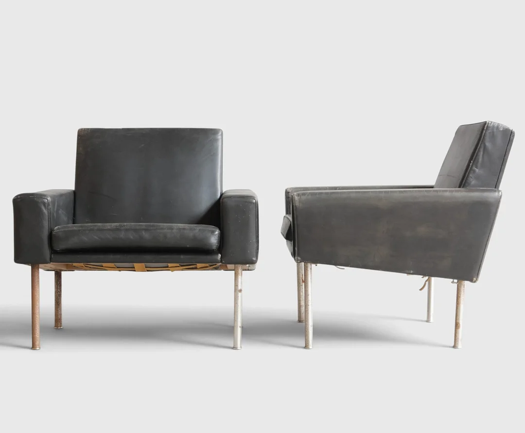 HANS J WEGNER. “Lufthavnsstolen”, et par lænestole med ben af stål, betrukket med sort kunstskind, løse sædehynder. Udført hos AP-stolen, model AP-34U. Danmark, 1960-70'erne (2). — Armchairs & Chairs — Woxholt Auktionshus