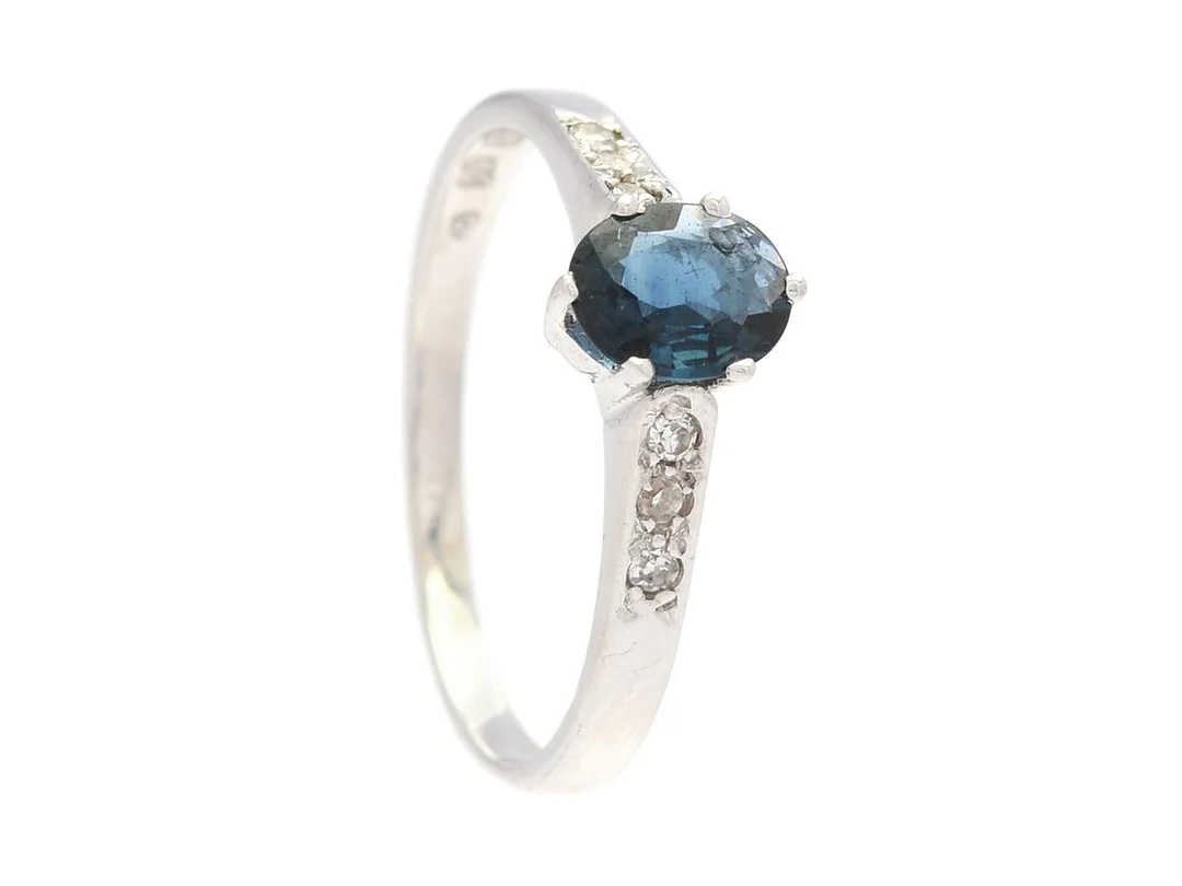 RING, 18K vitguld, ovalslipad safir, 6 åttkantslipade diamanter ca 0,06 ctv, stl 17,5 mm, vikt 2,4 g, safiren har en hålighet på undersidan. — Smycken/Ring — Kaplans