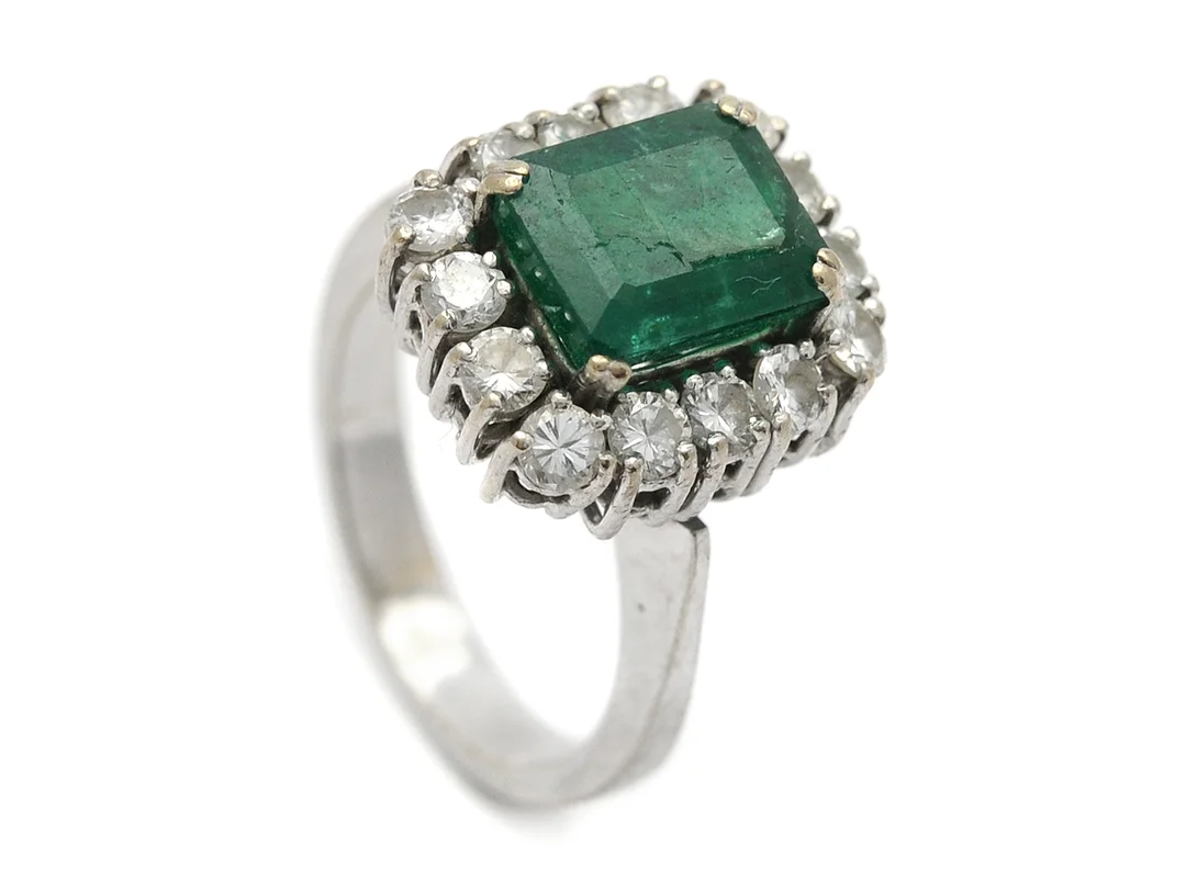 CARMOSÉRING, 18K vitguld, smaragd ca 2,60 ct, 14 briljantslipade diamanter ca 1,00 ctv, ca TW(G)/VS, stl 16 mm, vikt 7,5 g, spricka i smaragden, diamanter med aningen slitna fattningar. — Smycken/Ring — Kaplans