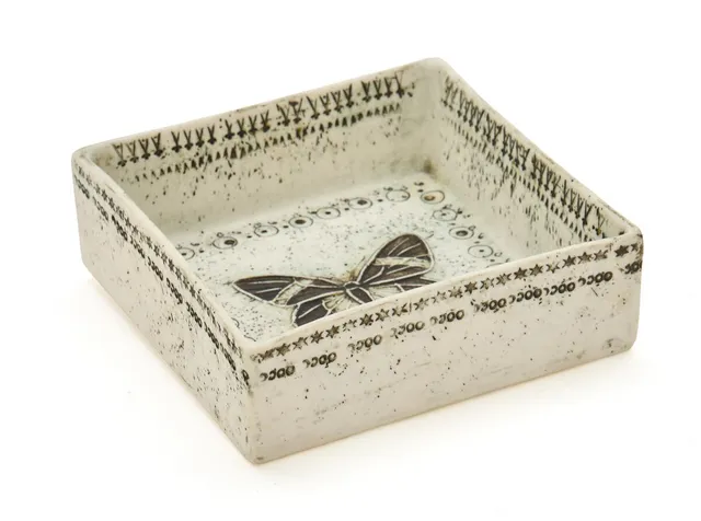 A small four-sided stoneware bowl with embossed motifs of a.o. a butterfly. Partially decorated with brownish-green glaze. Signed Bryk. Unique. H. 4 cm. W/L. 11.5 cm.