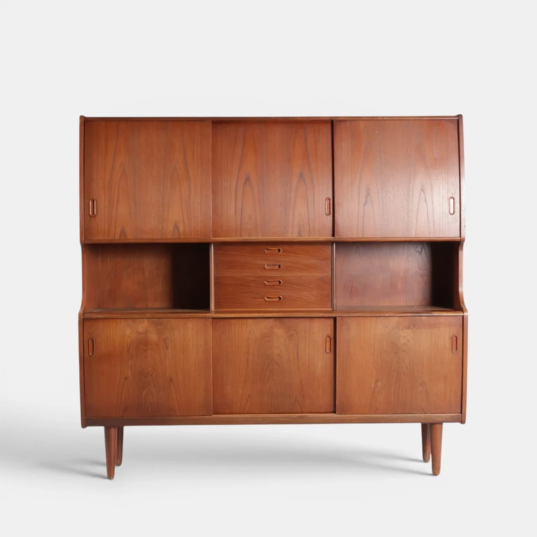 Skænk af teak, front med skuffer og skydelåger bag hvilke hylder, udtræksbakker og barsektion med spejlfelt, runde tilspidsede ben. Danmark, 1960'erne. — Cupboards, Cabinets & Shelves — Woxholt Auktioner