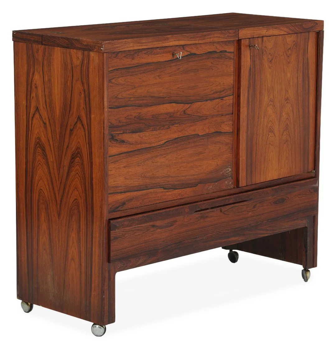 “Manhattan”. Bar cabinet of rosewood with partially opening top, partially drop-down front with black formica, and drawer. Interior fitted with mirror and glass shelf. Raised on four wheels. Manufactured for Bruksbo, 1960s. H. 99 cm. W. 110 cm. D. 45 cm. — Modern Furniture — Bruun Rasmussen