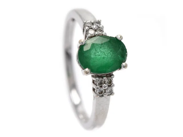 RING, 18K vitguld, ovalslipad smaragd ca 0,90 ct, 8 briljantslipad diamanter ca 0,08 ctv, ca W(H)/VS, stl 16,50 mm, vikt 2,7 g, smaragd med nagg på rondist och fasetterade kanter, samt inneslutning som når ytan.