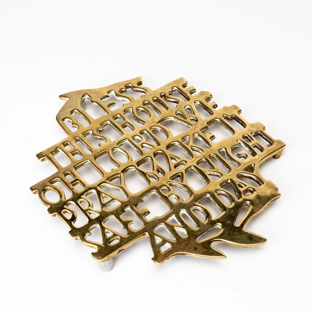 ESTRID ERICSON. Grytunderlägg, mässing, "Bless this house" för Firma Svenskt Tenn. — Pewter, Brass & Copper — Auktionshuset Kolonn