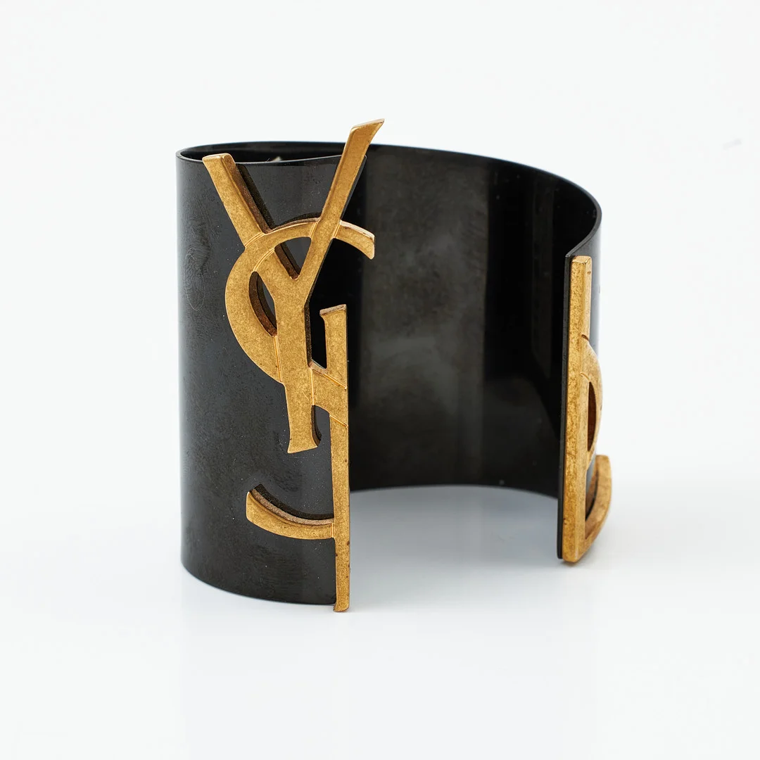 YVES SAINT LAURENT, armband, svartlackerad metall, logo i mässing, märkt invändigt "SAINT LAURENT PARIS". — Vintage & Designer Fashion — Stockholms Auktionsverk Magasin 5