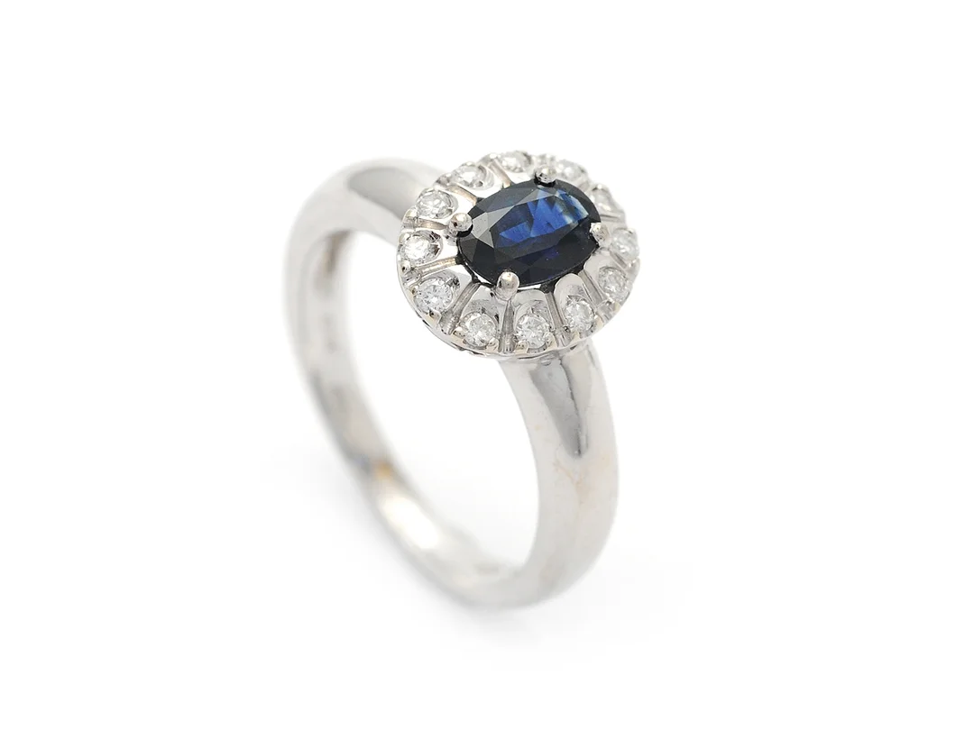 CARMOSÉRING, 18K vitguld, ovalt fasetterad blå safir, 12 briljantslipade diamanter ca 0,15 ctv, ca TCR/SI, inneslutning når ytan i en diamant, stl 17,75 mm, vikt 5,7 g. — Smycken/Carmoséring — Kaplans