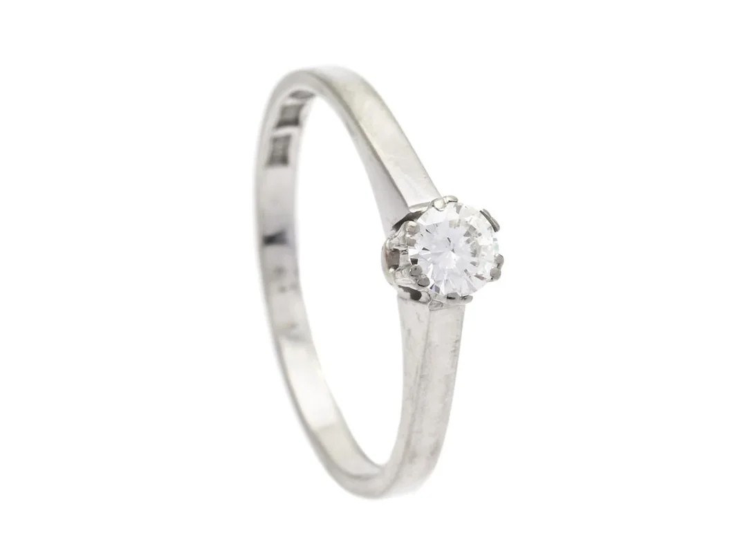 ENSTENSRING, 18K vitguld, briljantslipad diamant 0,15 ct enligt gravyr, ca TW/VS, John Petterssons eftr, Stockholm 1964. stl 15,5 mm, vikt 1,8 g, slitna fattningar samt en klo med skada. — Smycken/Enstensring — Kaplans
