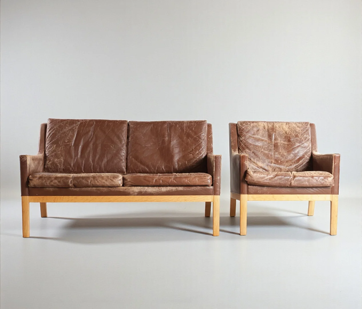 KAI LYNGFELDT LARSEN (F. 1919, D. 1976). Fritstående to-pers. sofa med tilhørende lænestol, ben af eg, betrukket med brunt skind. Udført hos Søren Willadsen. Danmark, 1960-70'erne (2). — Sofas & Seatings — Woxholt Auktioner