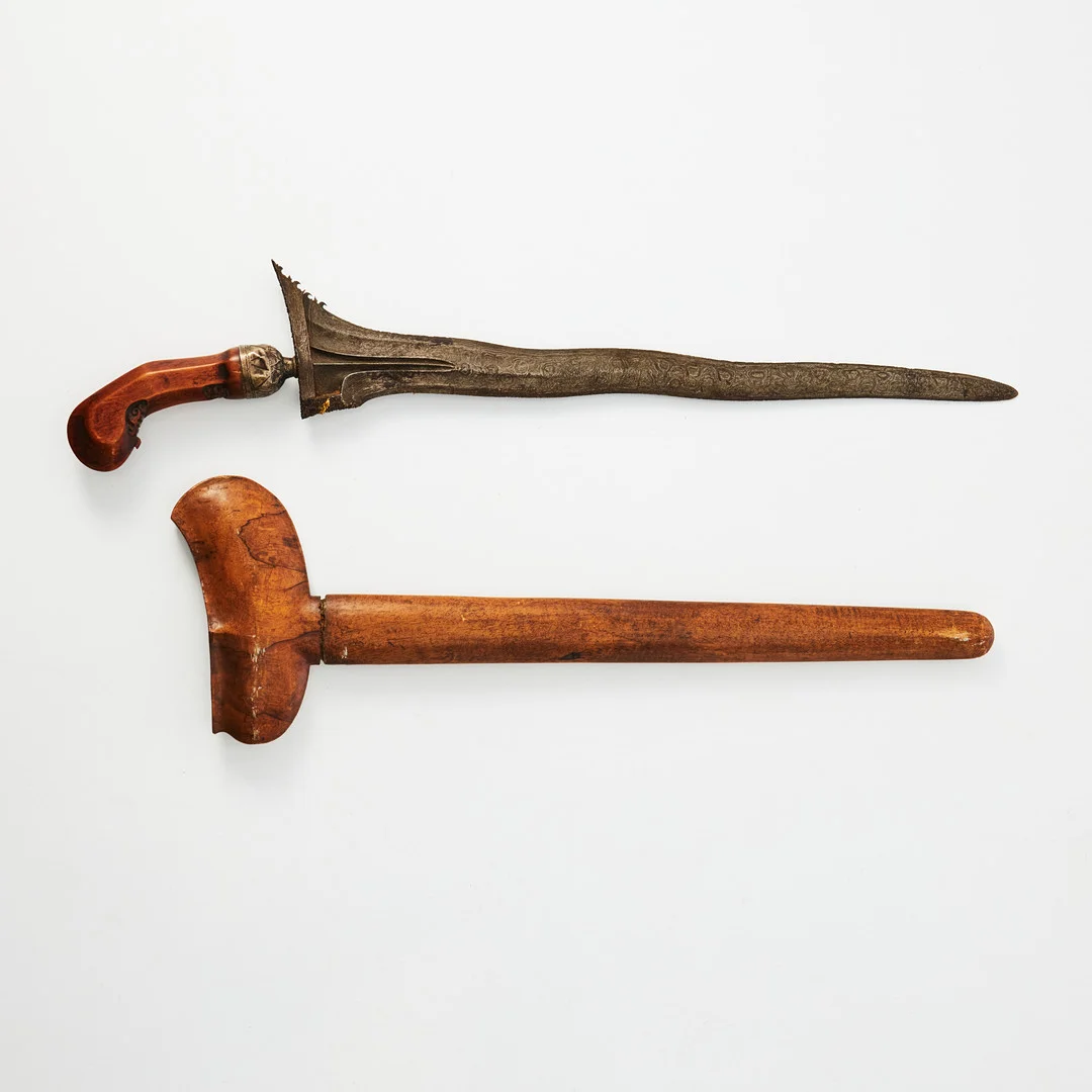 KRIS, Indonesien, möjligen Bali, 1800-tal, vågformigt blad i damaskerat stål, fäste i trä med skuren dekor med beslag i låghaltigt silver. — Edged weapons — Stockholms Auktionsverk Magasin 5
