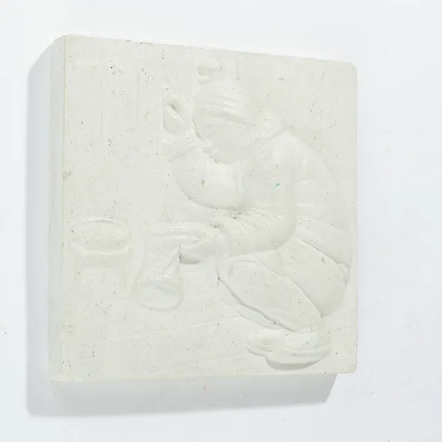Bemalet gipsrelief med motiv af inuit syende en støvle, signeret med monogram af ubekendt billedhugger, 1900-tallets anden halvdel.