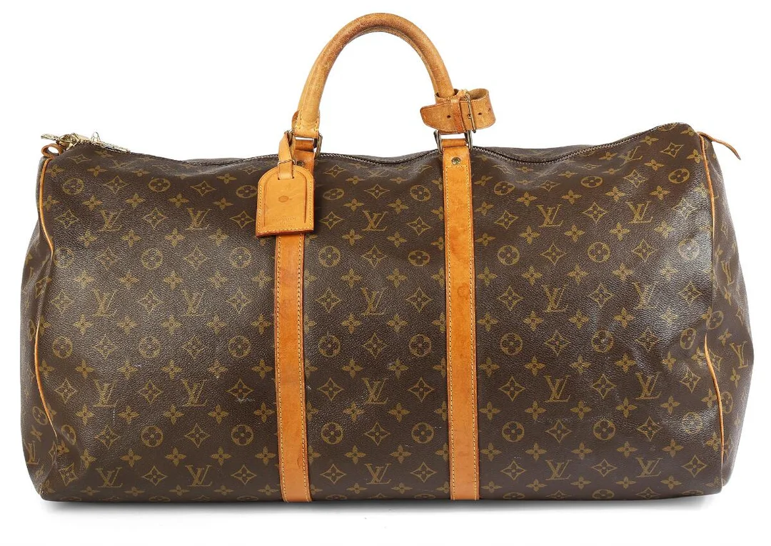 A “Keepall” travel bag of brown monogram coated canvas with brown leather trim, gold-toned hardware, two handles, one buckle on the handle, one luggage-tag, one zipped compartment with brown fabric lining. H. 30 x W. 60 x D. 40 cm. 1993. — Designer Handbags & Fashion/Designer Handbags — Bruun Rasmussen
