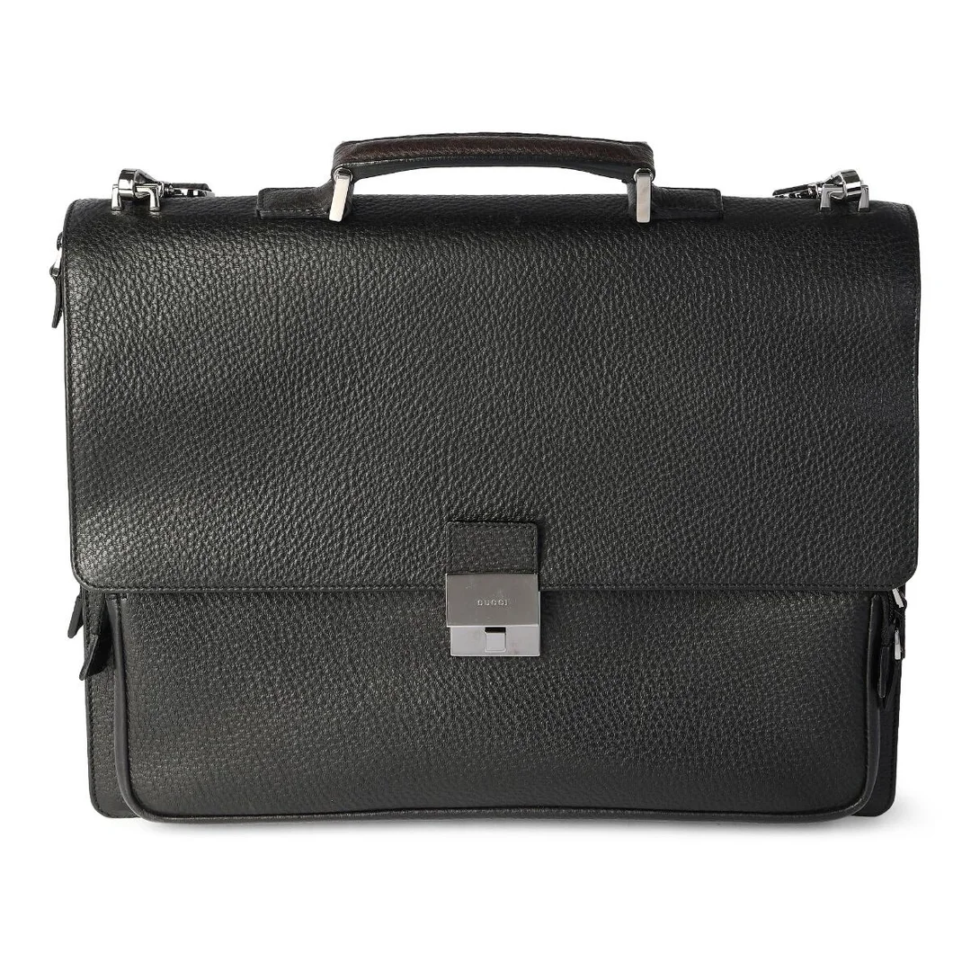 A briefcase/bag in black leather with silver tone hardware, short handle, detachable and adjustable shoulder strap, one exterior back pocket, one front zipped pocket underneath flap, two interior compartments divided by a zipped pocket, an additional zipped pocket, a pen holder and black fabric lining. H. 32 x W. 40 x D. 10 cm. — Designer Handbags & Fashion/Designer Handbags — Bruun Rasmussen