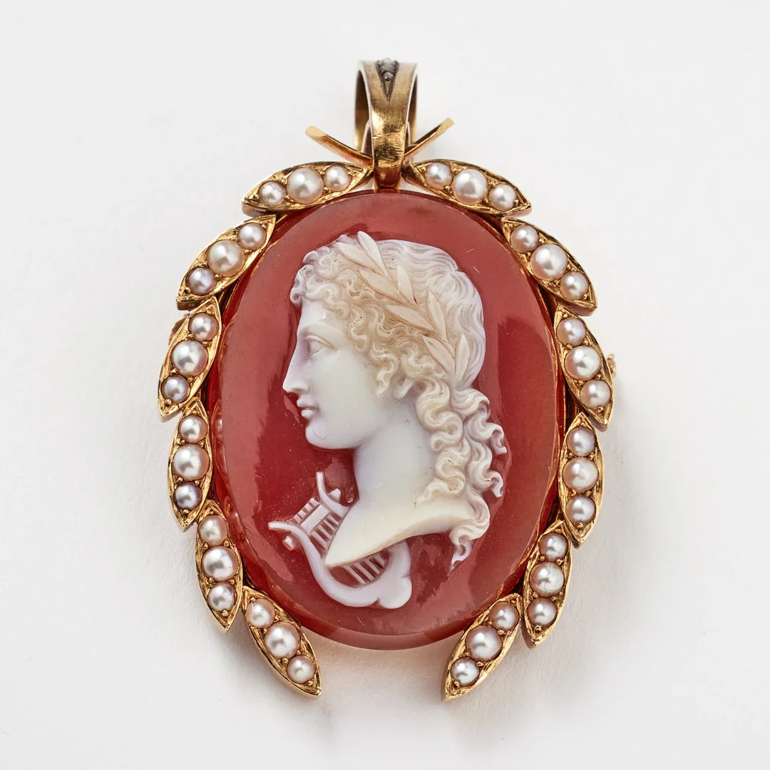LARS LARSON (1844-1880), brosch/hänge, 18 k guld, röd sardonyx med skuret porträtt av Apollo, avbildad med lagerkrans samt lyra, bård med orientaliska pärlor, upphäng med dekor av rosenslipade diamanter, baksida med gömma. — Brooches & Pendants — Stockholms Auktionsverk Fine Art