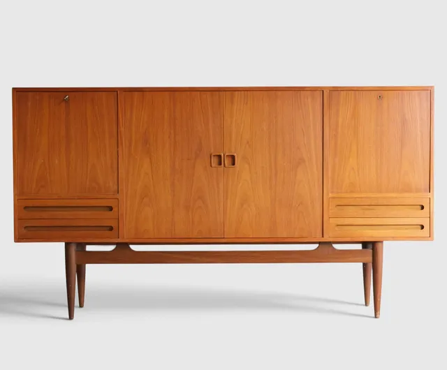 EJVIND A. JOHANSSON. Skænk af teak, front med skuffer, låger og nedfældige låger bag hvilke udtræksbakker og barsektion med spejlglas og hylder af farvet glas, stel med runde tilspidsede ben. Danmark, 1960'erne.