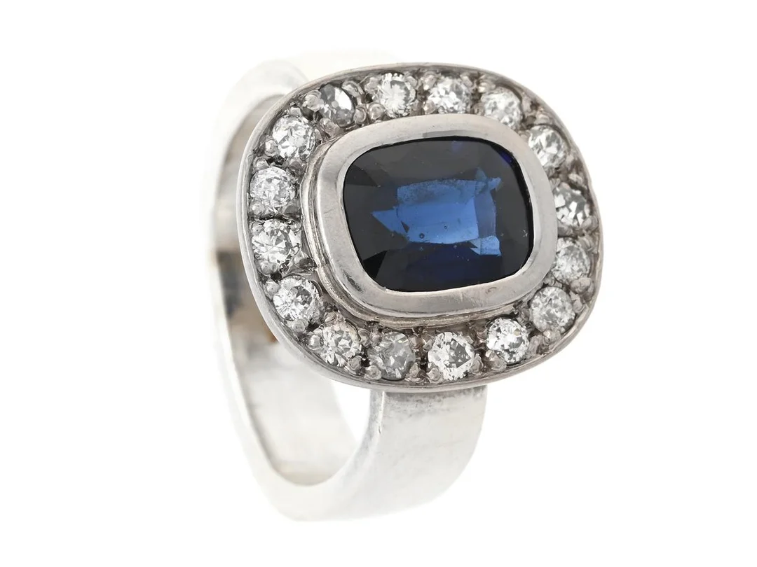 RING, 18K vitguld, kuddslipad syntetisk safir, diamanter ca 0,70 ctv, stl 17,5 mm, vikt 10,6 g, senare ringskena i sterlingsilver av Helena Edman, Stockholm 2013, svaga fattningar, enstaka diamanter har nagg och skador, safiren har slitna fasettkanter och nagg. — Smycken/Ring — Kaplans