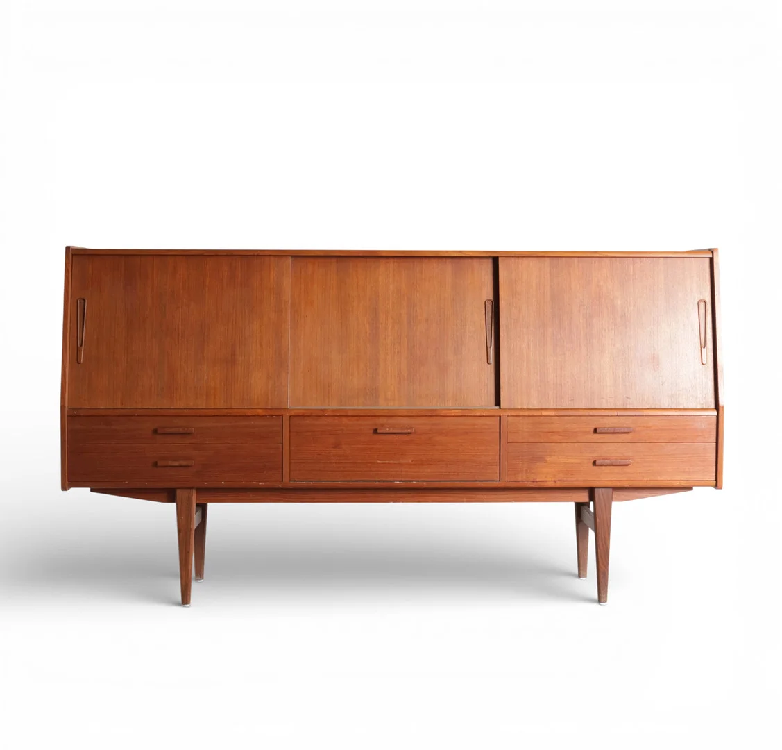 Skænk af teak, buet front øverst med tre skydelåger, bag hvilke hylder og barindretning med spejlfelt herunder skuffer med messinggreb, stel med tilspidsede ben. Udført hos ES Møbler, Silkeborg. Danmark, 1960'erne. — Cupboards, Cabinets & Shelves — Woxholt Auktioner