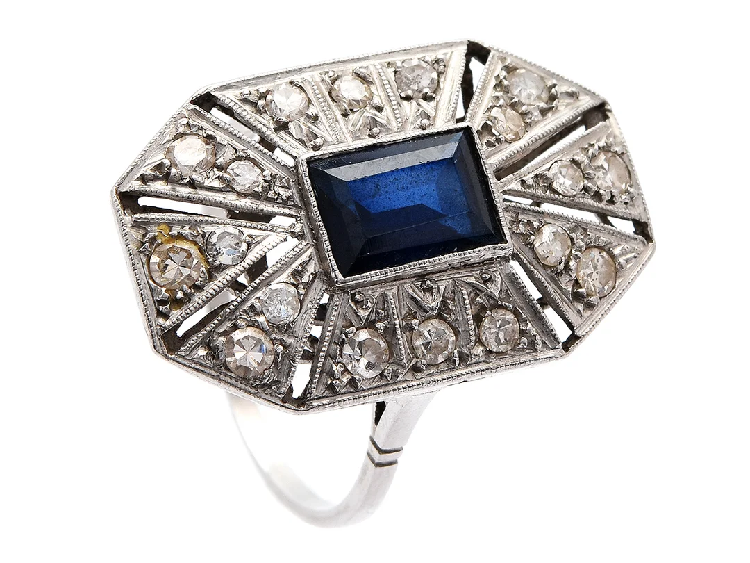 RING, platina, 1 trappslipad syntetisk saifr, 16 åttkantslipade diamanter ca 0,30 ctv, 1900-talets första hälft, stl 16,75 mm, vikt 4,7 g, något slitna fattningar. — Smycken/Ring — Kaplans
