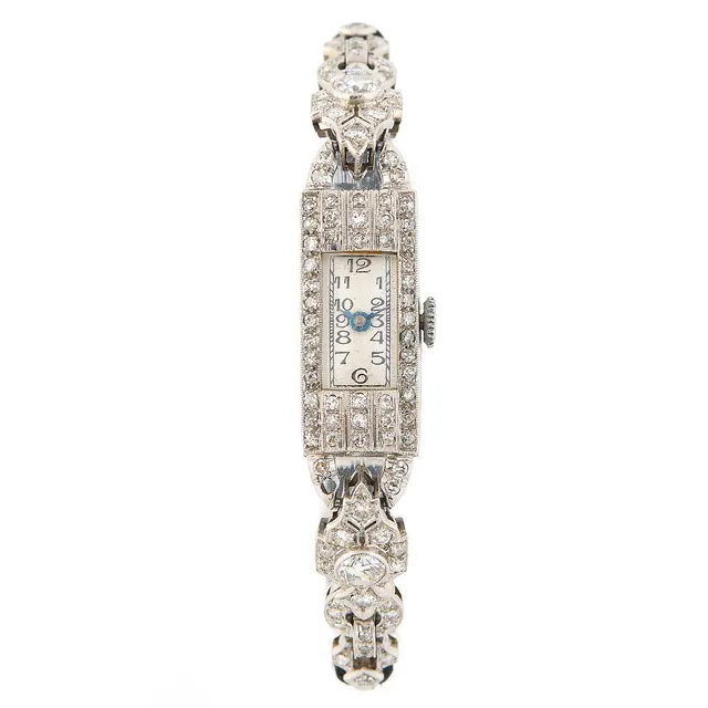 “Art Deco” of platinum. Mechanical movement with manual winding and diamond-set bezel and bracelet. Black fabric strap with lol fold-over clasp of steel. Circumference approximately 15.5 cm. 11×31 mm. 1930s.