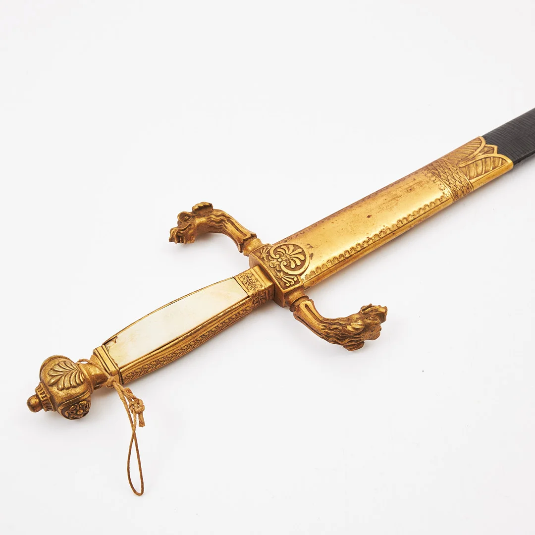 ÄMBETSMANNAVÄRJA, 1800-tal, klinga med ås, skulpterat fäste med parerstänger formade till odjurshuvuden, kavelplattor av pärlemor, svart läderbalja med beslag. — Edged weapons — Stockholms Auktionsverk Magasin 5