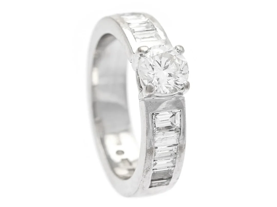 RING, 18K vitguld, briljantslipad diamant ca 0,55 ct, ca W(H)/SI, 14 baguetteslipade diamanter ca 0,58 ctv, ca W/VS, Stockholm 2006, stl 15,5 mm, vikt 6,8 g, en bagutteslipad diamant med skada. — Smycken/Ring — Kaplans