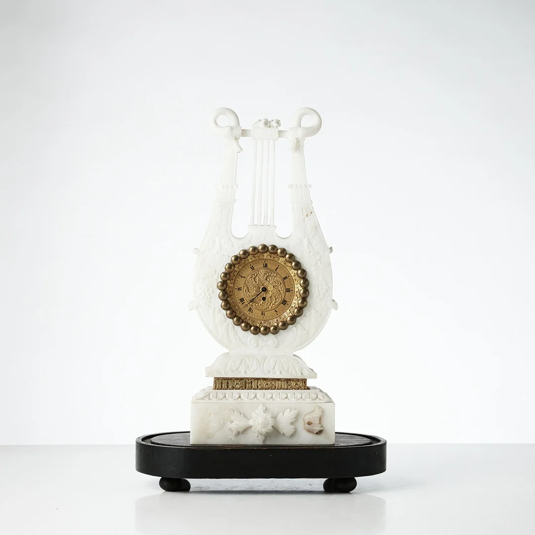 BORDSUR, senempire, alabaster, skuren dekor i form av lyra, urtavlan delvis förgylld, romerska siffror, på alabastersockel samt på träsockel. — Mantel clocks — Stockholms Auktionsverk Magasin 5