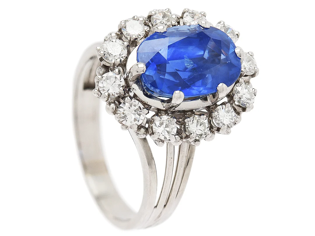 CARMOSÉRING, 18K vitguld, ovalslipad safir ca 3,60 ct, 12 äldre briljantslipade diamanter ca 0,60 ctv, ca TW-Cr/VS, stl 17 mm, vikt 7,9 g, en diamant med nagg på kuletten. — Smycken/Carmoséring — Kaplans