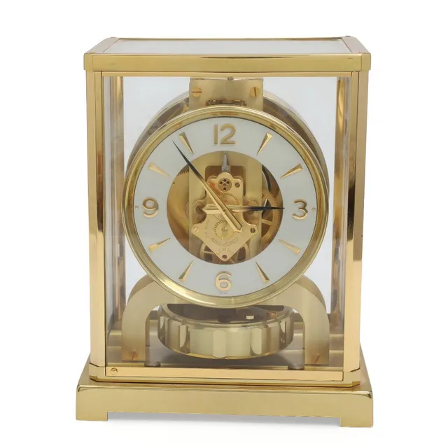“Atmos”. A gilt brass and glass table clock with visible movement, dial with Arabic numerals. Marked ATMOS. Serial number 148889. Mid 20th century. H. 22.5. L. 18. W. 13.5 cm.