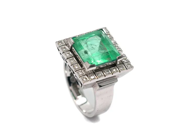 RING, 18K vitguld, smaragd ca 7,26 ct (enl gravyr), nagg i ett hörn, inneslutningar som når ytan, 24 åttkantslipade diamanter ca 0,30 ctv, ca TW/VS, tillv av Ceson i Göteborg 1970, stl 17,25 mm, vikt 13,0 g.