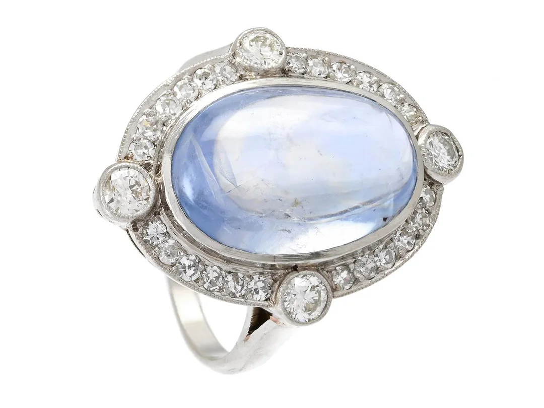 CARMOSÉRING, platina, cabochonslipad safir ca 10,60 ct, 4 briljant- och 24 åttkantslipade diamanter ca 0,54 ctv, ca TW-Cr/VS-P, Stockholm 1947, storlek 17,25 mm, vikt 9,1 g, safiren har inneslutning som når ytan, enstaka diamanter har nagg och skador. — Smycken/Carmoséring — Kaplans