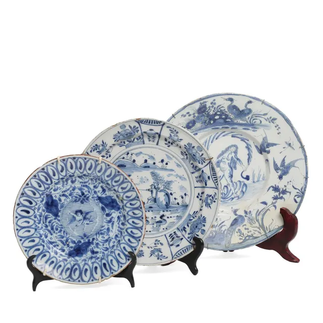 Three Delft blue and white faience dishes, decorated with central motifs of a chreub, Venus born of waves and a fishing man. 17th-18th century. Diam. 26–34 cm. (3)