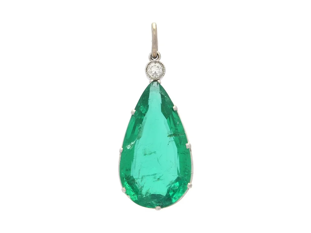 HÄNGE, platina, droppslipad smaragd ca 4,32 ct, gammalslipad diamant ca 0,05 ct, ögla i 18K vitguld, höjd 25 mm, vikt 2,5 g, smaragden med inneslutningar som når ytan samt skador vid rondist. — Smycken/Hänge — Kaplans