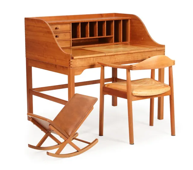 A freestanding solid cherry wood writing desk, front with storage room and three drawers, table top with two small flaps and one larger, middle flap covered with natural leather. And an armchair upholstred in seat with natural leather. And a rocking footstool with brown leather. Manufactured respectively by Hadsten Møbelindustri and Form75. H. 103. L. 111. W. 82 cm. (3)