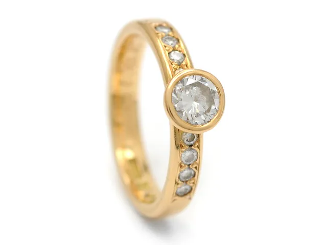 RING, 18K guld, briljantslipad diamant 0,39 ct enligt gravyr, ca W/skadad, i övrigt mycket små inneslutningar, 8 briljantslipade diamanter 0,16 ctv enligt gravyr, ca W/VS, Guldbolaget i Bergkvara, stl 15 mm, vikt 3,3 g, gravyr.
