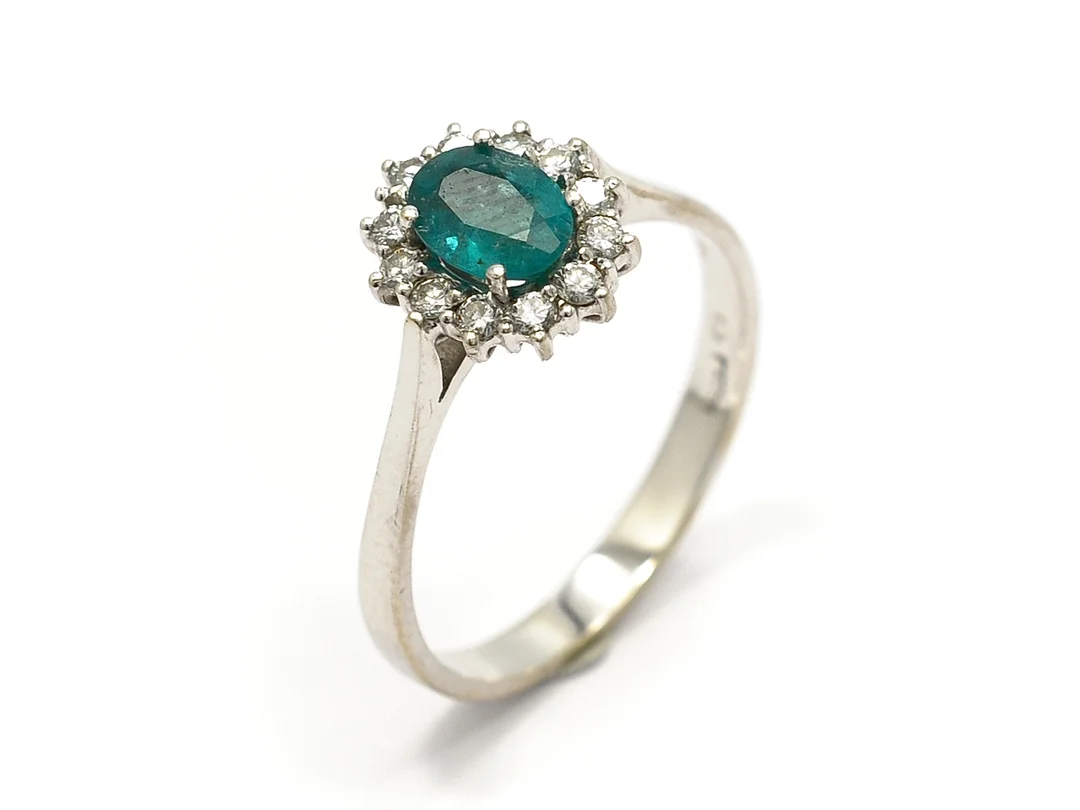 CARMOSÉRING, 18K vitguld, smaragd, sprickor som når ytan, små skador, 12 briljanter ca 0,24 ctv, ca W/VS, en skadad, stl 19 mm, vikt 3,6 g. — Smycken/Carmoséring — Kaplans