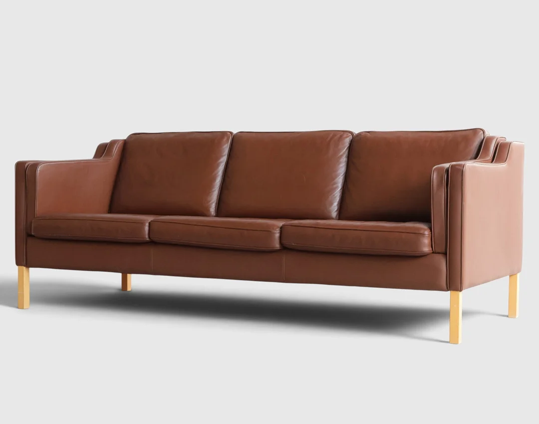 Fritstående tre-personers sofa med ben af bøg, betrukket med læder, løse hynder i sæde, ryg og sider. Udført og mærket hos Stouby, model "Eva". Danmark, 20. årh. anden halvdel. — Sofas & Seatings — Woxholt Auktionshus