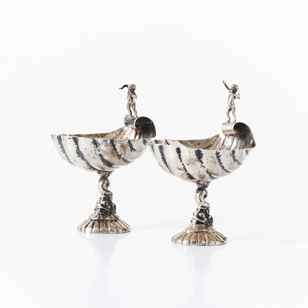 SALTKAR, ett par, silver, 1900-talets början, i form av snäckor med putto, fot med delfin, svenska importstämplar. — Silver — Stockholms Auktionsverk Magasin 5