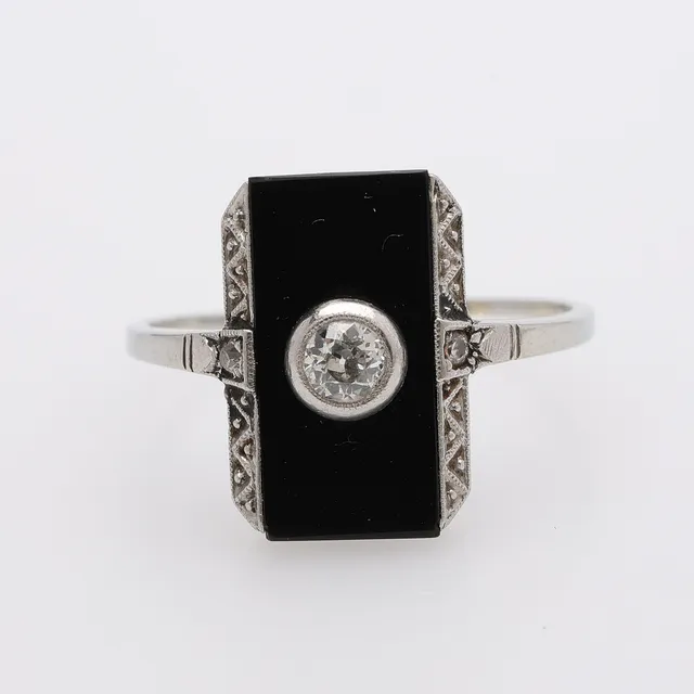 DIAMANTRING, 18 k vitt guld, art déco, med en gammalslipad briljant om ca 0,20 ct i infattning på flack svart onyx och 2 små rosenstenar. 1910/20-tal.