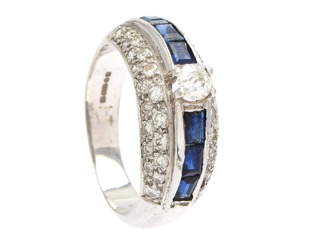 RING, 18K vitguld, 39 briljantslipade diamanter ca 0,55 ctv, ca W-Cr/SI-P, 6 fasetterade safirer, stl 16,75 mm, vikt 6,0 g, några diamanter och safirer med ytdefekter, mittstenen har inneslutning som når ytan. — Smycken/Ring — Kaplans
