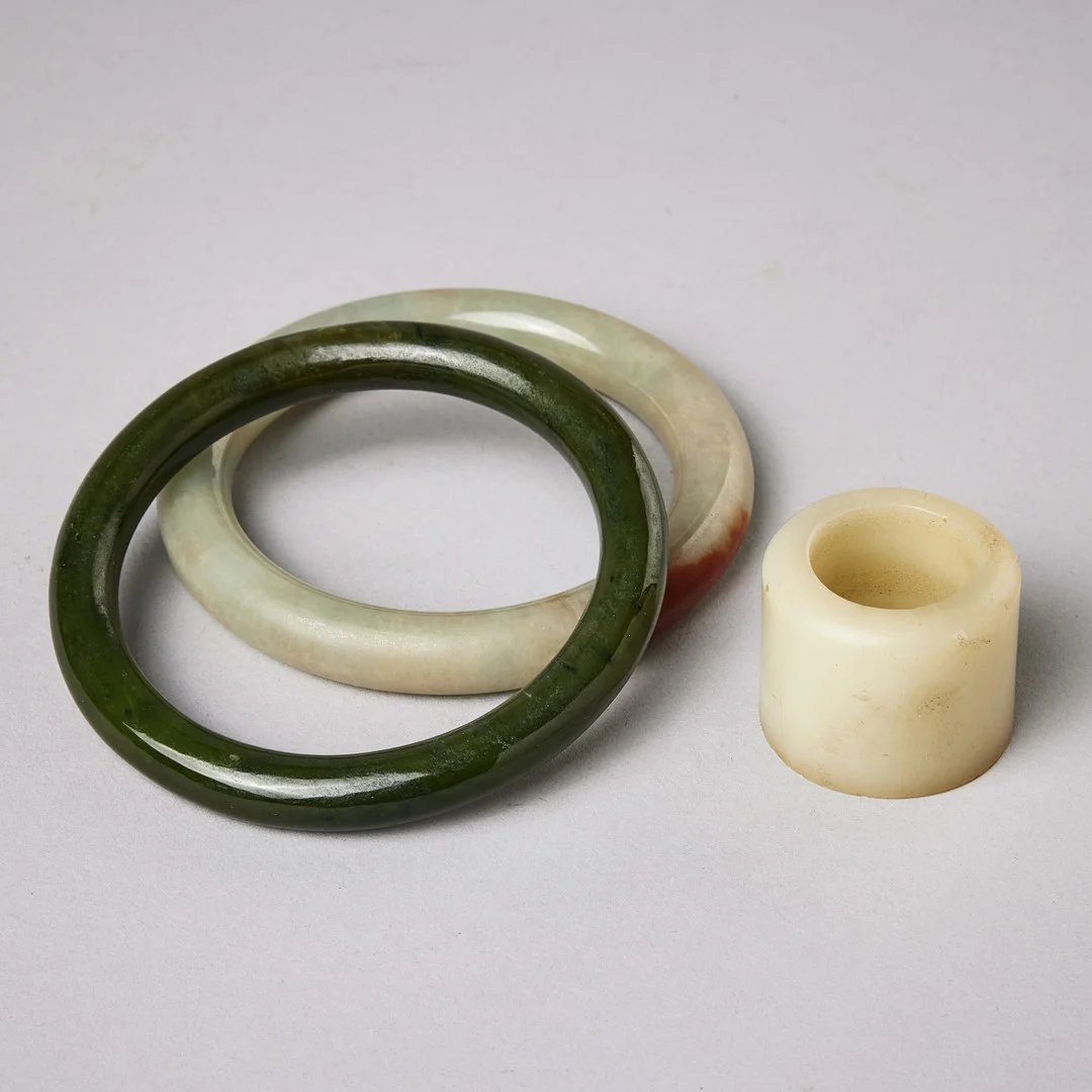 A PALE CELADON JADE ARCHERS RING, A MOSS GREEN NEPHRITE BANGLE AND A JADE BANGLE WITH A REDDISH SPOT. — Asiatica — Stockholms Auktionsverk Fine Art