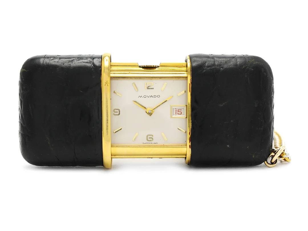 MOVADO, Ermeto, Boett nr. E576 519, fickur, 40 x 25 mm (utfälld 61 mm), doublé / läder, manuell, plexiglas, datum, ca 1960, kedja i gulmetall. Klockan dras upp genom att öppna och stänga fodralet. — Klockor/Movado — Kaplans