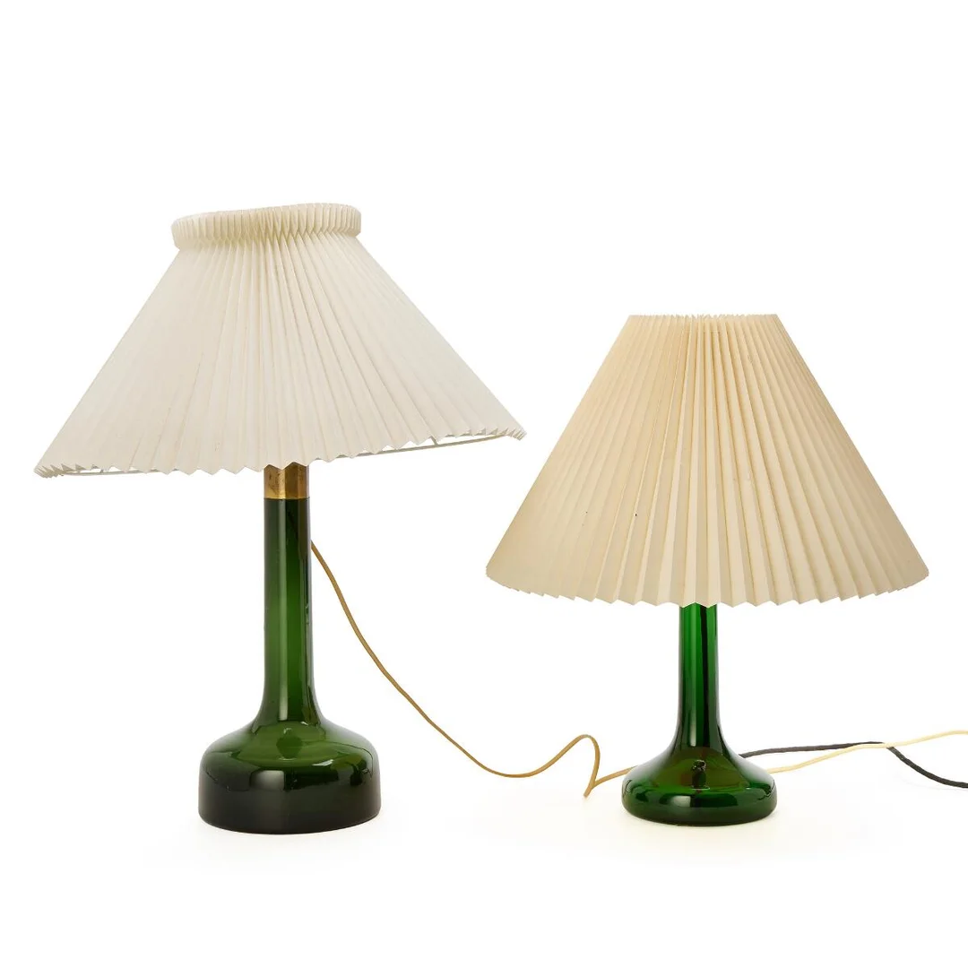 Two table lamps of green glass with brass mountes. Pleated paper shades. Model 343 and 302. Made by Holmegaard for Le Klint. H. including shades 50 and 61 cm. (2) — Modern Decorative Art — Bruun Rasmussen
