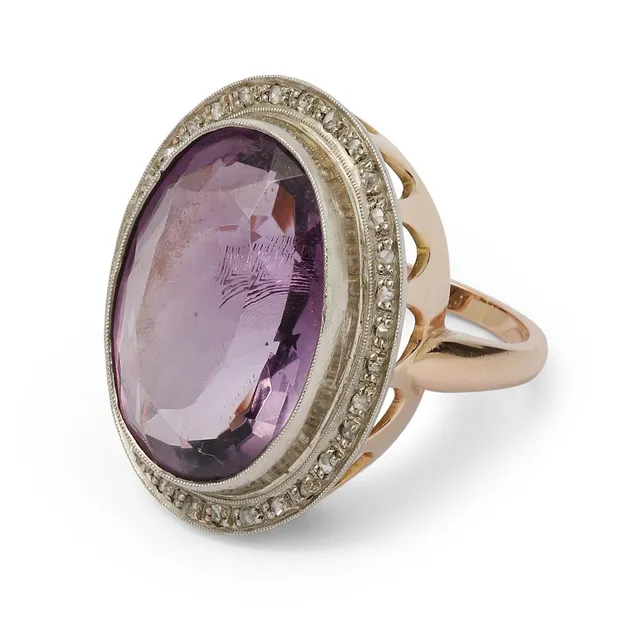 An amethyst ring set with an oval-cut amethyst encircled by numerous rose-cut diamonds, mounted in 14k gold and palladium. Weight app. 15.5 g. W. 3 cm. Size 58.