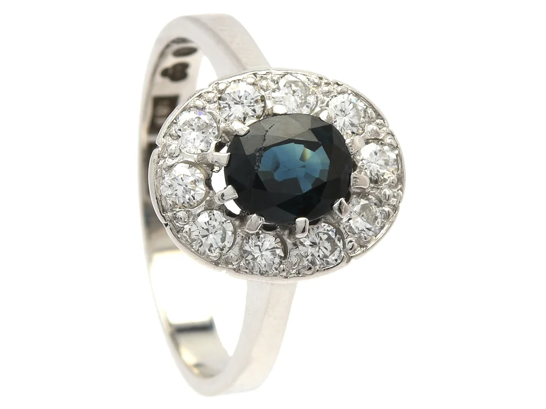CARMOSÉRING, 18K vitguld, ovalslipad blå safir ca 0,78 ct, 10 briljant- och äldre briljantslipade diamanter ca 0,46 ctv, ca TW-TCr(G-I)/SI, stl 17 mm, vikt 4,6 g, safiren har nagg vid bordet, en diamant med nagg vid bordet och en med nagg på kulett. — Smycken/Carmoséring — Kaplans