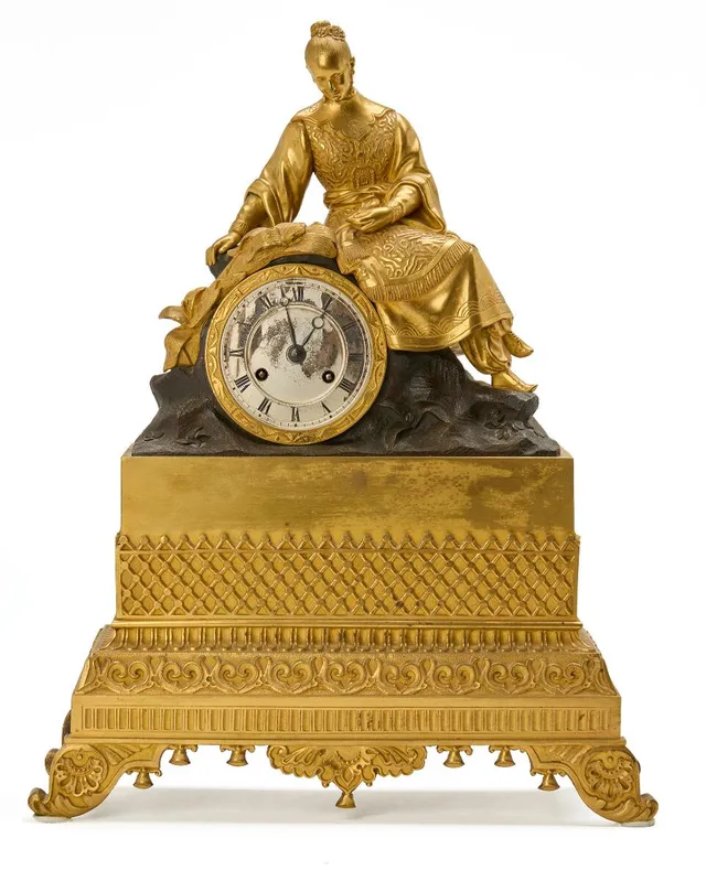 Fransk Louis Philippe kaminur af forgyldt og patineret bronze, urhus med siddende ung asiatisk kvinde, forsølvet skive. 19. årh.s første halvdel. H. 41. B. 31.