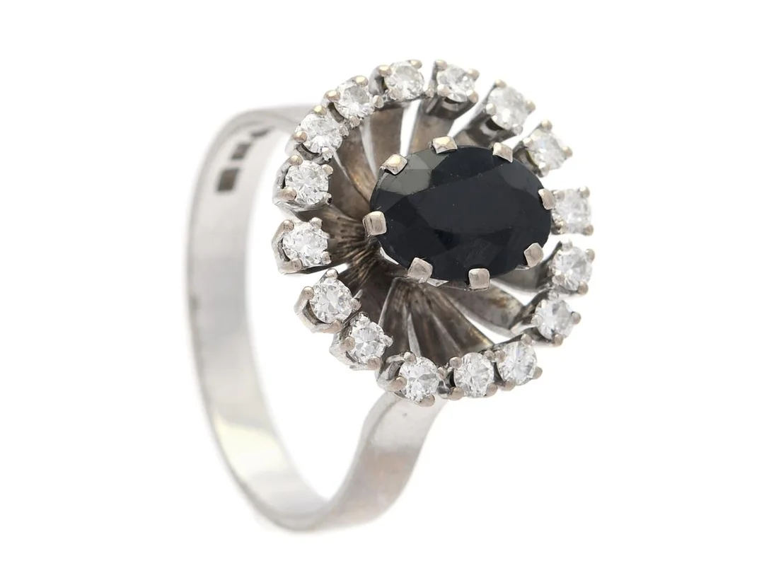 RING, 18K vitguld, ovalslipad safir, 16 briljantslipade diamanter ca 0,48 ctv, ca TW-W/VS-SI, stl 20 mm, vikt 9,1 g, safiren har mindre nagg och slitna fasetter, en diamant är skadad. — Smycken/Ring — Kaplans