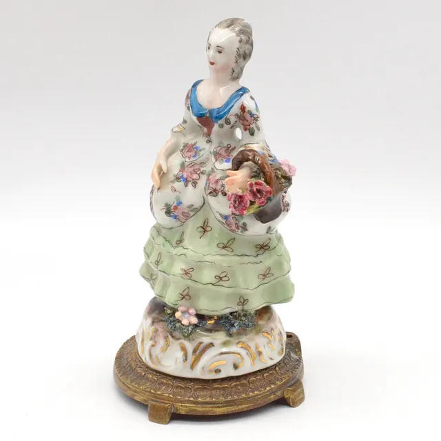 "FRAU MIT BLUMENKORB", FRANZÖSISCHE TAFELDEKORATION AUS PORZELLAN, POLYCHROM MIT GOLDMALEREI, AUF BRONZESOCKEL MONTIERT, UM 1850.
