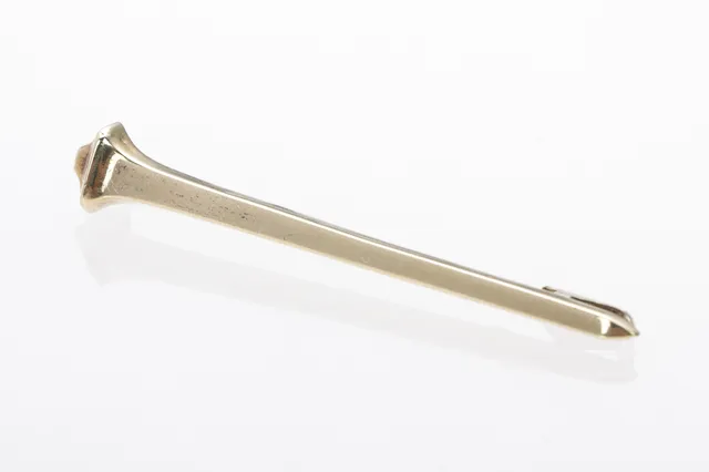 B. Hertz: A brooch of 14k gold in the shape of a horseshoe nail.