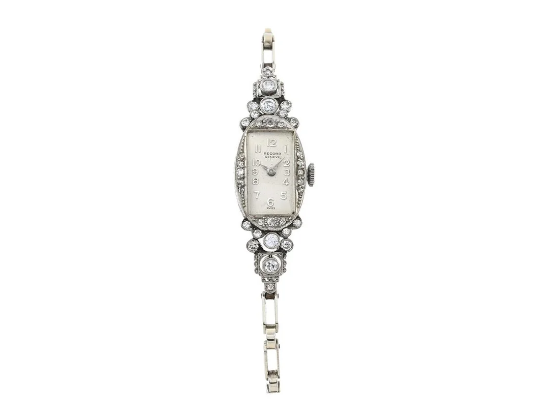 DAMUR, "Record, Geneve", 14,5 x 47 mm, Cal 143, Boett nr. 43761, platina, manuell, plexiglas, skadad urtavla, formverk, diamanter/briljanter på boetten (38 st. ca 0,80 ctv), boett signerad Eszeha, integrerad länk i 18K vitguld, längd 165 mm, ca 1940. — Klockor/Record — Kaplans